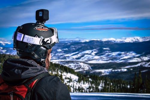 头盔与动作相机看着雪山的男人 · 免费素材图片