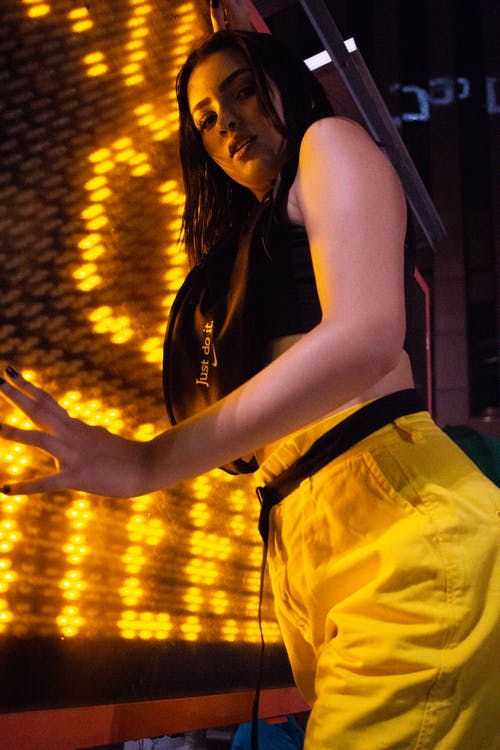 女人穿着黑色运动胸罩和黄色的裤子，在黄色霓虹灯前摆姿势的照片 · 免费素材图片