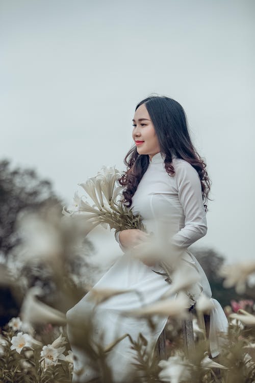 女人穿着白色高领长袖连衣裙拿着花瓣花瓣 · 免费素材图片