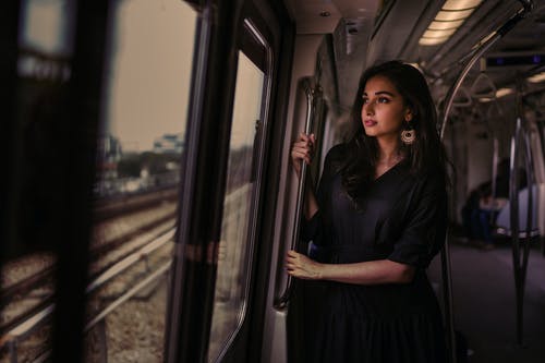 站在火车里看着外面的女人站在金属轨道上的女人的照片 · 免费素材图片