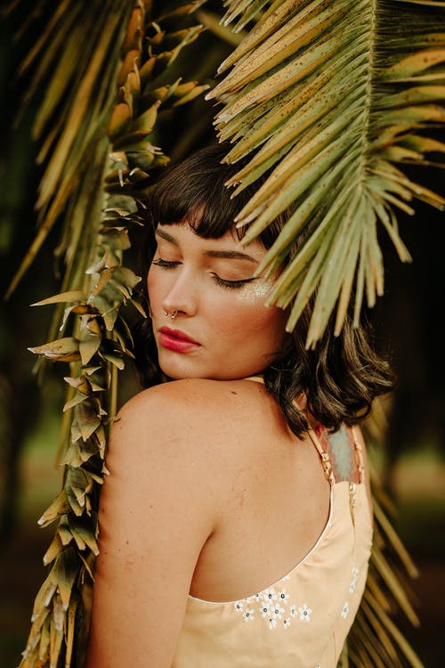 闭着眼睛站在棕榈叶下的女人的照片 · 免费素材图片