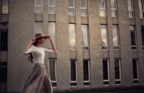 手持太阳帽走在混凝土建筑外面的女人的照片 · 免费素材图片