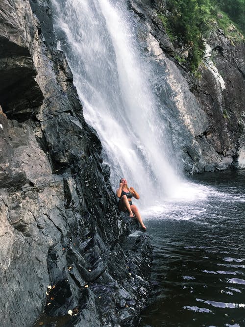 坐在瀑布附近的岩石上的人 · 免费素材图片