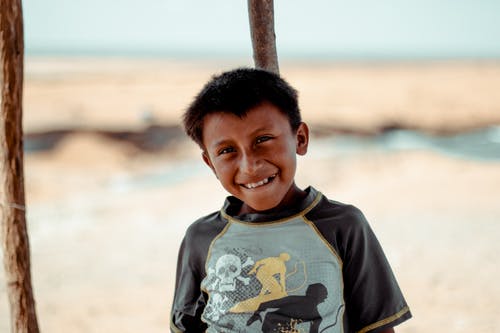 倾斜在木杆的微笑的男孩照片 · 免费素材图片