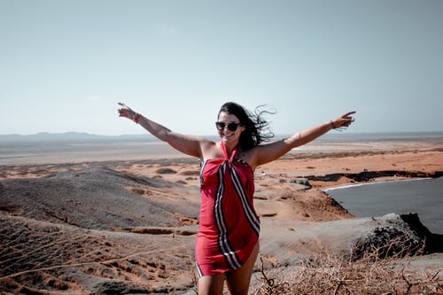穿红色和白色吊带裙站在沙丘中间的女人 · 免费素材图片