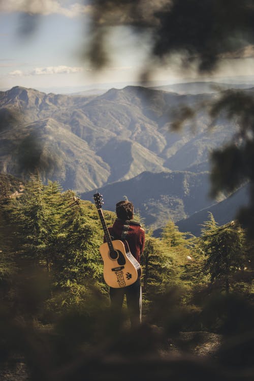 有站立在绿色领域的原声吉他的人在山附近 · 免费素材图片