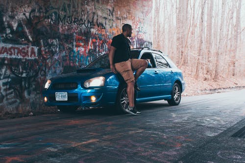 男子坐在停泊的蓝色5门斯巴鲁掀背车引擎盖上的照片 · 免费素材图片