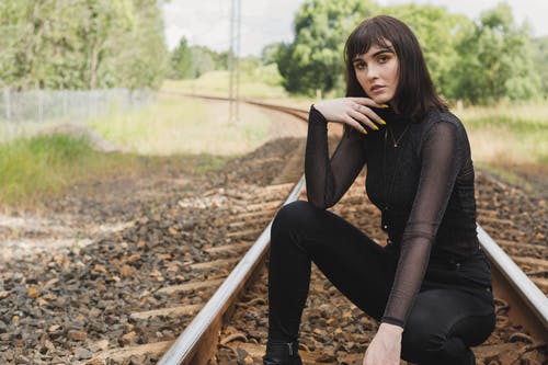 在火车轨道中间摆姿势的黑衣服蹲的女人的照片 · 免费素材图片