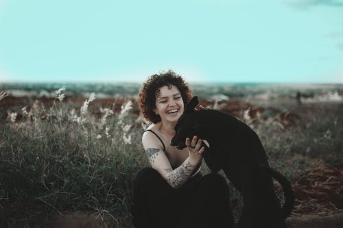 微笑的女人抚摸着黑狗的照片 · 免费素材图片