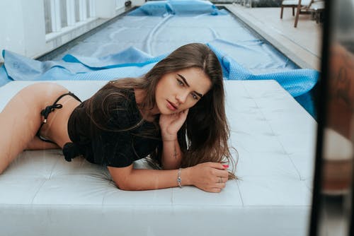 黑色t恤和比基尼底部躺在白色皮革池畔沙发上的女人的照片 · 免费素材图片