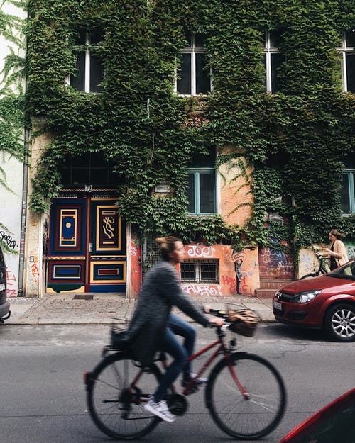 骑自行车与绿色藤蔓的混凝土房子旁边的人 · 免费素材图片