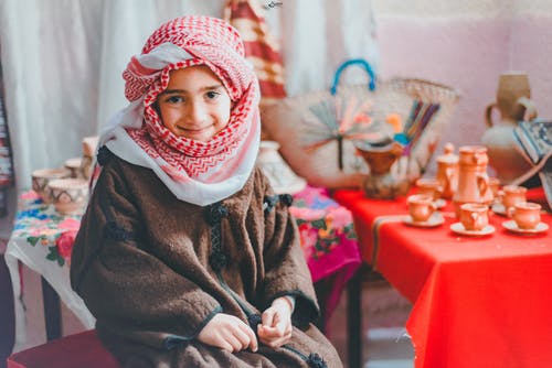 白色和红色的keffiyeh围巾和棕色夹克坐在微笑的男孩的照片 · 免费素材图片