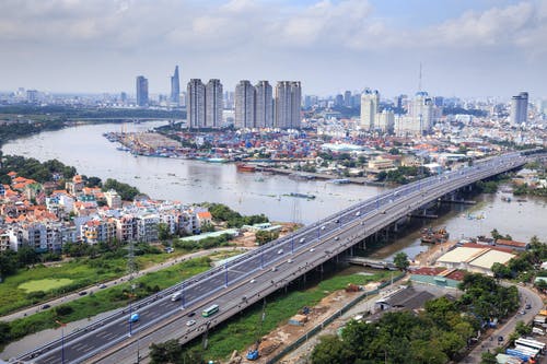 高层建筑显示桥梁和大海附近的道路上的不同车辆 · 免费素材图片