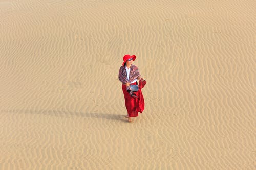 女人穿着红色的裙子在空旷的沙漠上行走 · 免费素材图片