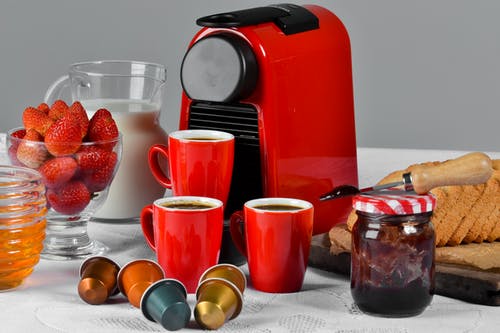 红色陶瓷杯装满咖啡在桌子上的果酱罐附近 · 免费素材图片