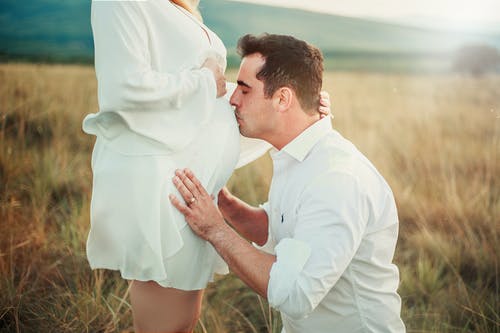 男人亲吻孕妇的肚子在绿色的田野 · 免费素材图片