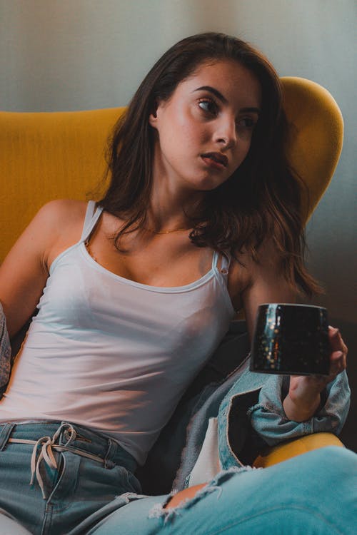坐在白色的背心，拿着咖啡杯摆姿势的坐在女人的照片 · 免费素材图片