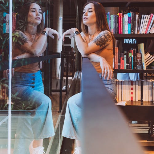 站在靠近玻璃墙的棕色背心和蓝色牛仔牛仔裤的女人 · 免费素材图片