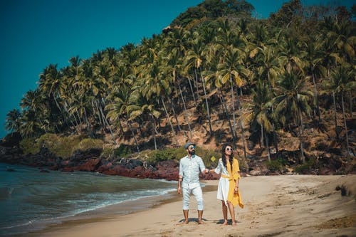 男人和女人站在海边附近的山上长满了椰子树 · 免费素材图片