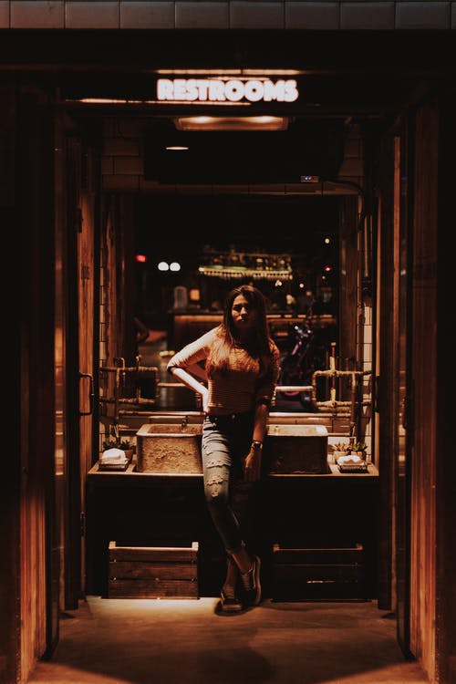 女人穿着牛仔牛仔裤站在洗手间霓虹灯下 · 免费素材图片