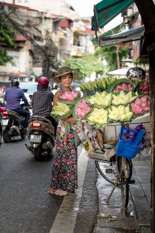 女人站在路边和建筑物附近的鲜花 · 免费素材图片