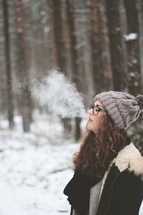 站立和在积雪覆盖的森林上吸烟的女人 · 免费素材图片