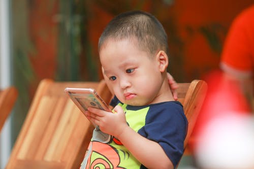 男孩抱着椅子上的智能手机选址 · 免费素材图片