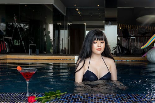 女人在游泳池附近的葡萄酒和红玫瑰花朵杯上穿着黑色比基尼上衣 · 免费素材图片