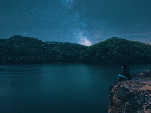 晚上坐在平静的水面峰顶上的女人 · 免费素材图片