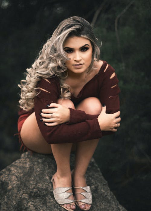 褐红色的长袖上衣，同时握住双腿坐在岩石上的女人 · 免费素材图片