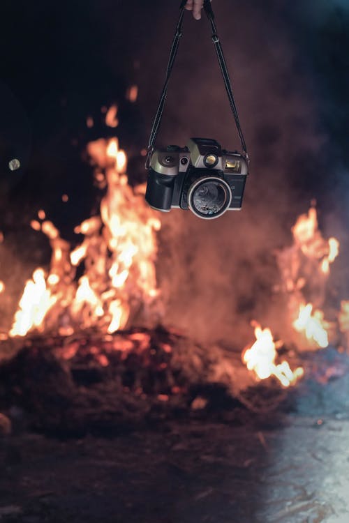 拿着黑色和灰色照相机在火附近的人 · 免费素材图片
