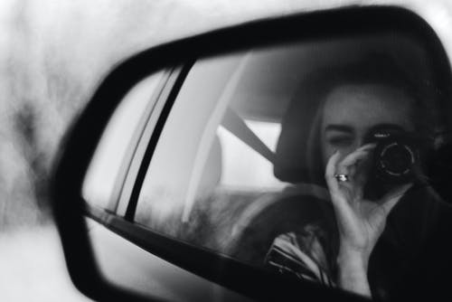 女人在车辆后视镜手持相机拍摄的灰度摄影 · 免费素材图片