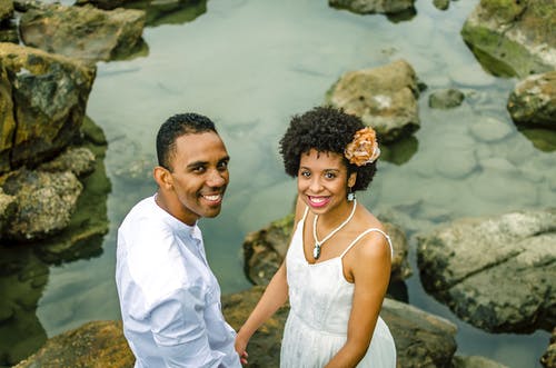 微笑对夫妇的照片穿着白色的手牵着手，而站在岩石上的水体 · 免费素材图片