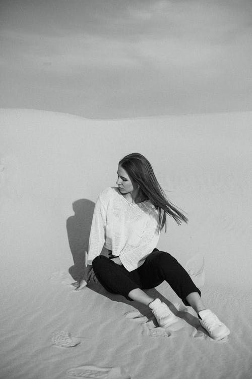 女人坐在沙滩上的灰度摄影 · 免费素材图片