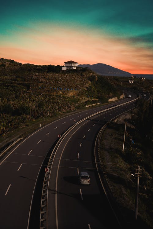 灰色的车，在绿色和橙色的天空下不停的高速公路上行驶 · 免费素材图片