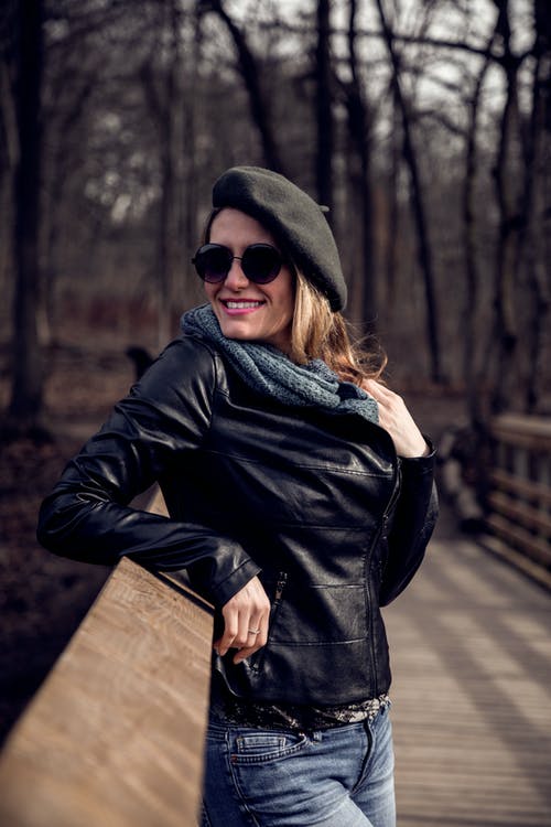 黑色皮夹克站在微笑时站在棕色木桥上的女人 · 免费素材图片