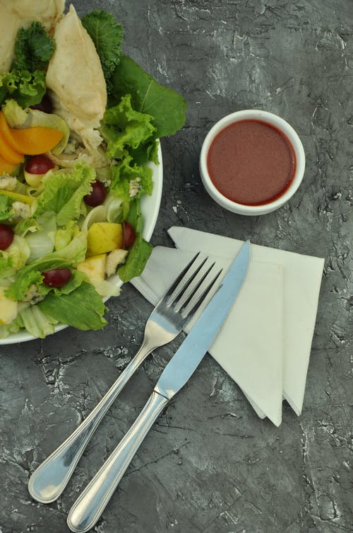 银叉和面包刀在板上的蔬菜沙拉附近 · 免费素材图片