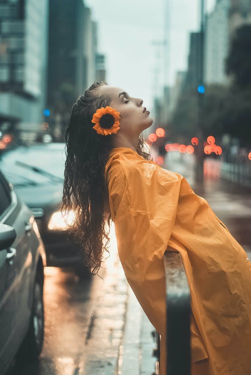 黄色的雨衣，靠在人行道上的黑色金属栏杆上的女人的照片 · 免费素材图片