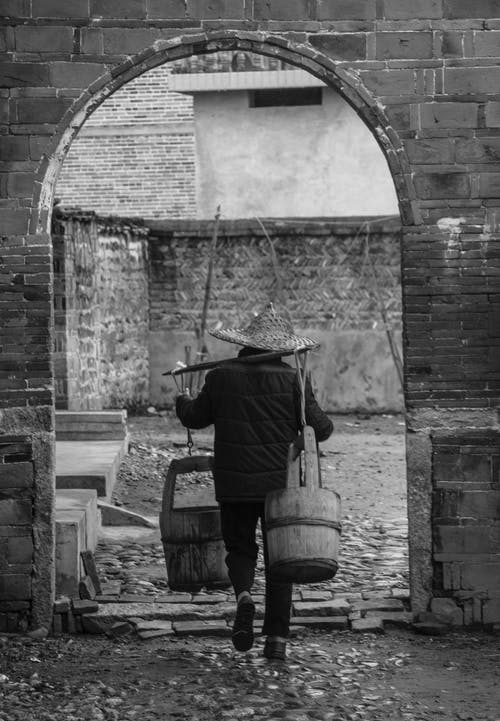 黑白摄影中的男子携带桶 · 免费素材图片