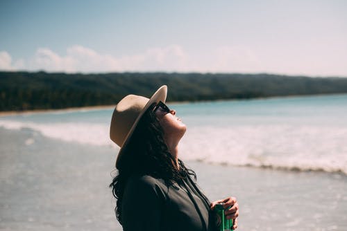 戴着米色帽子站在海边看着一边的女人 · 免费素材图片