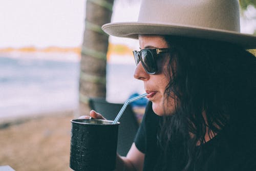 戴着墨镜在黑杯上喝酒的女人的浅焦点照片 · 免费素材图片