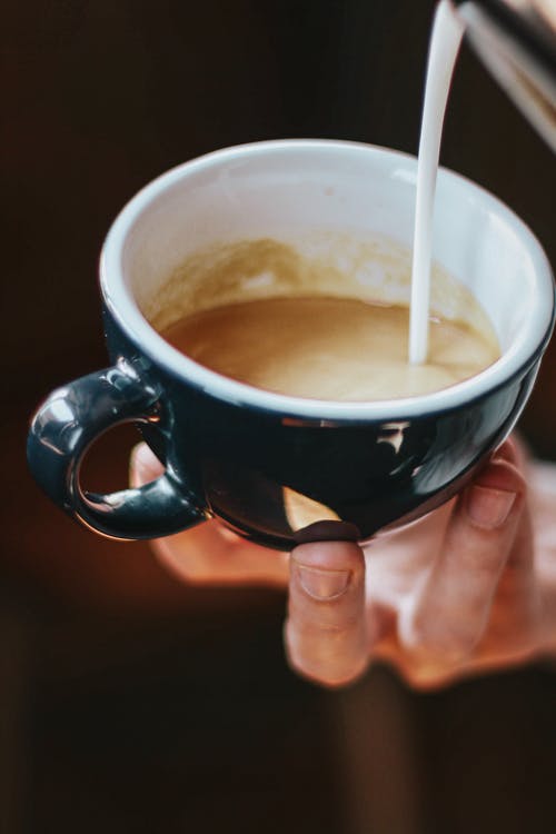 人在杯子上倒牛奶的特写照片 · 免费素材图片