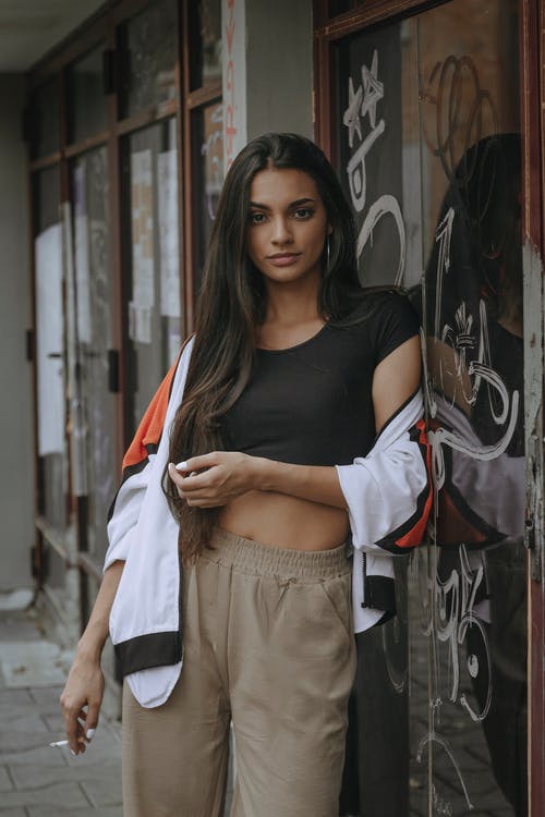 靠在玻璃门，拿着香烟的女人的照片 · 免费素材图片