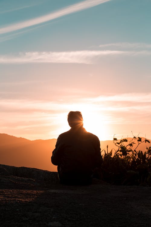 人在日落期间坐着和面对山的轮廓 · 免费素材图片