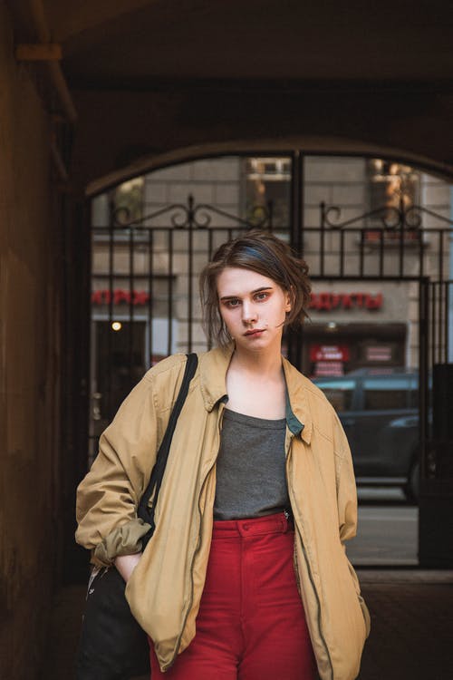 穿着棕色拉链外套和红色长裤摆姿势的女人的照片 · 免费素材图片