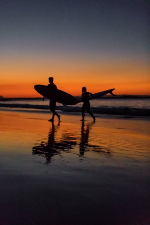 日落期间在海边的两个冲浪者 · 免费素材图片