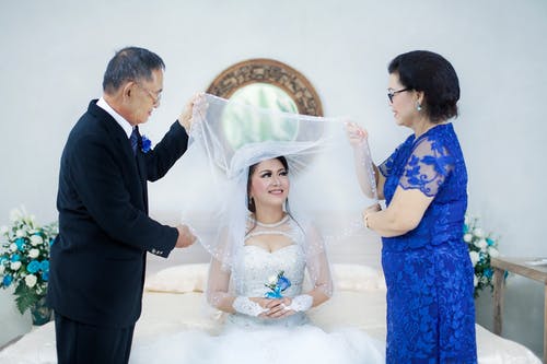 穿着正式西装的男人和穿着蓝色连衣裙的女人之间的婚纱的女人 · 免费素材图片