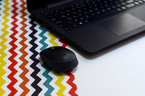 笔记本电脑旁边的黑色无线鼠标 · 免费素材图片