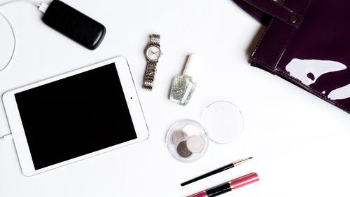 白色ipad，银色手表，黑色智能手机，指甲油瓶和白色背景上的黑色化妆刷 · 免费素材图片