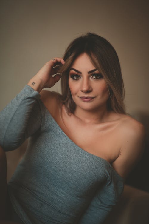 女人穿着灰色长袖露肩连衣裙用手在头发上 · 免费素材图片